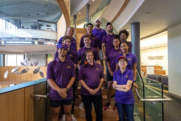 group of people in purple polos stand on stairs in BEC